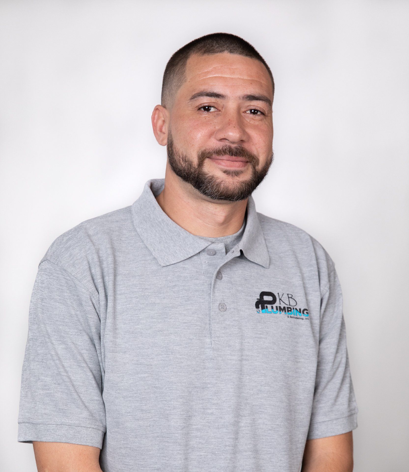 Man with short dark hair and a beard wearing a grey polo shirt with a logo, smiling slightly.