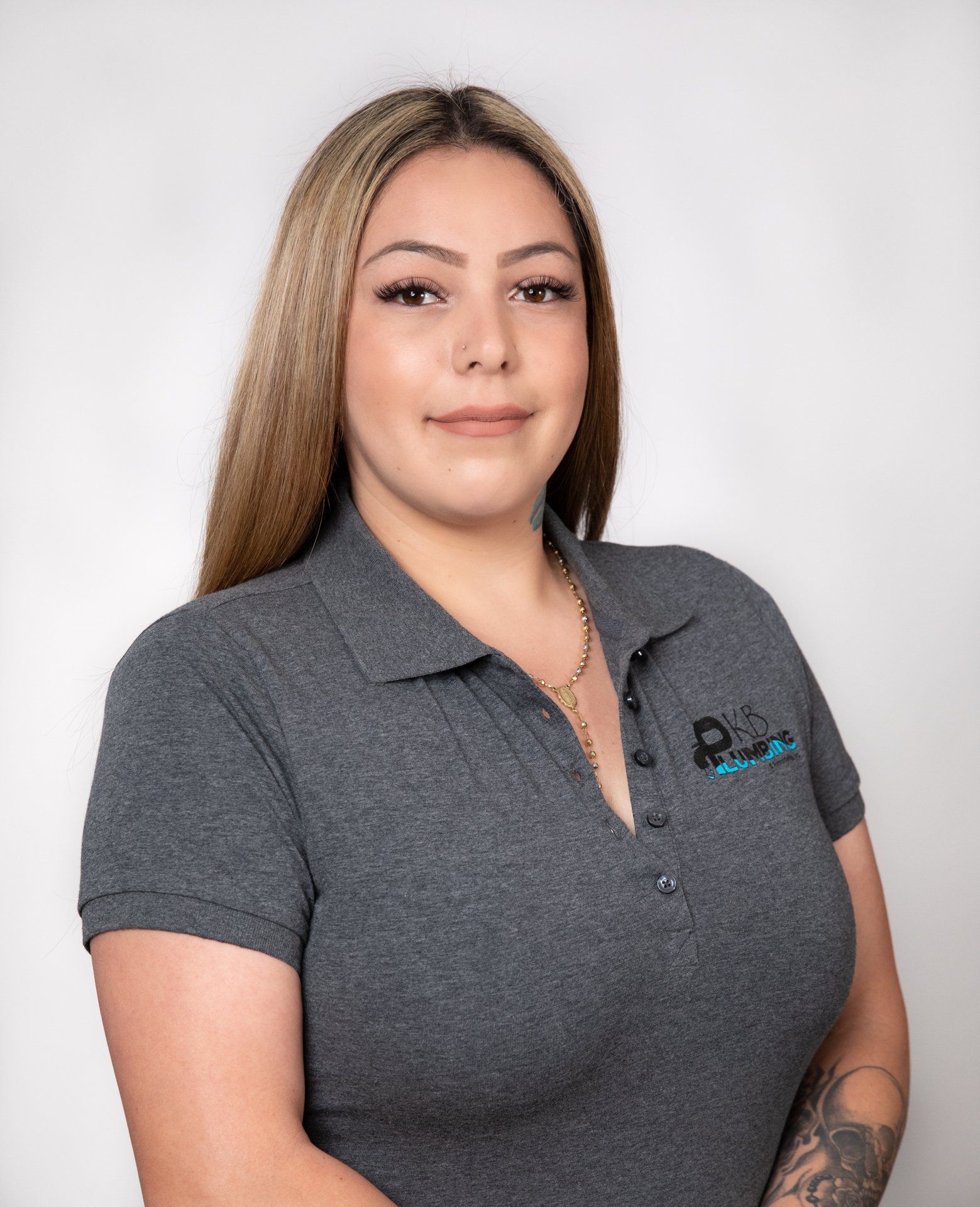 Woman wearing a gray polo shirt, smiling, with long blonde hair, standing in front of a white backdrop.