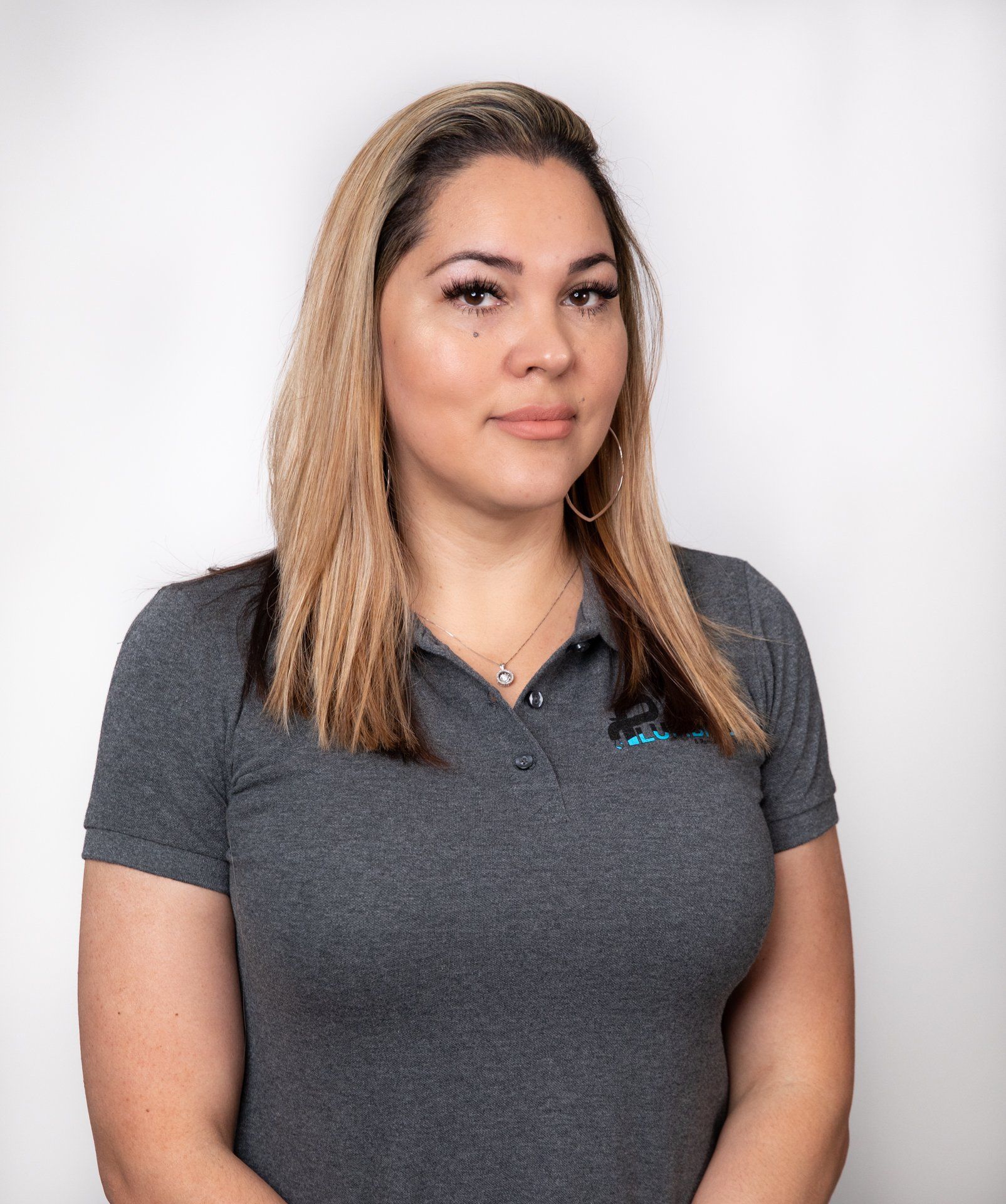 Woman with long blonde hair in a gray polo shirt, looking at the camera against a white backdrop.