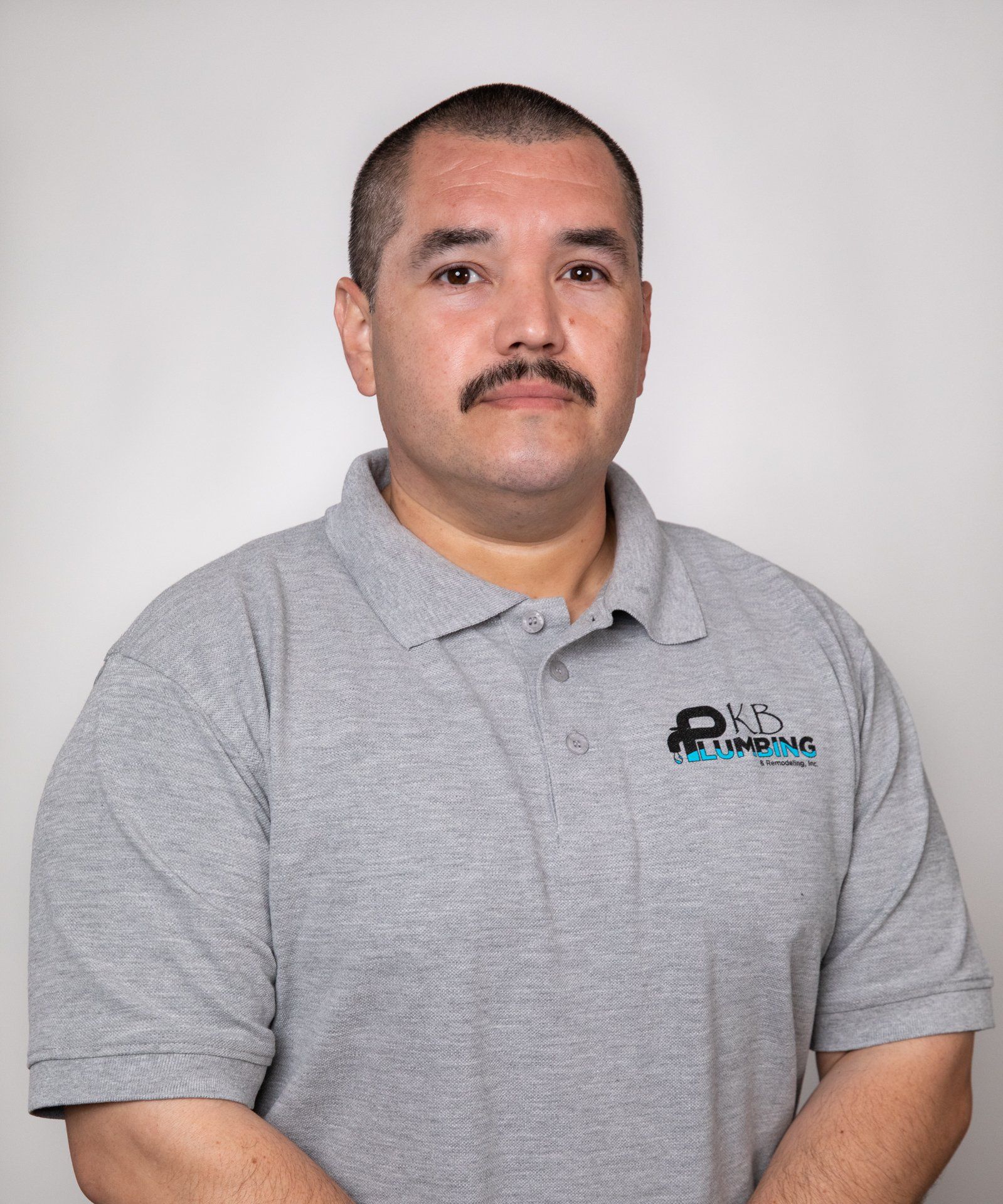 Man wearing a gray polo shirt with a logo, standing in front of a white backdrop.