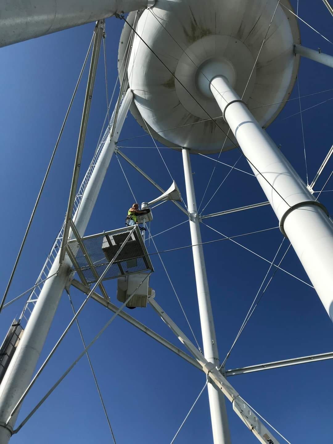 Woman in straw hat smiles, holding wine glass near a lake.