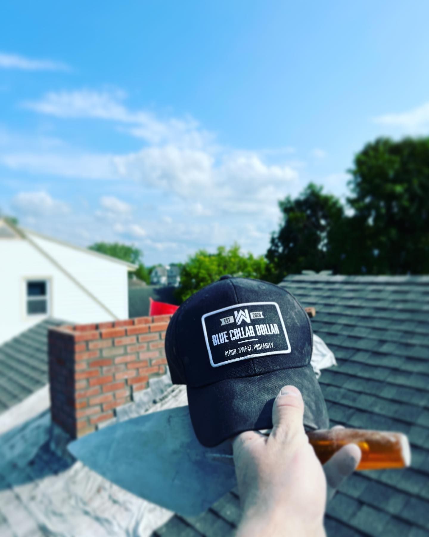 Hand holding a trowel with a black cap on it, on a rooftop with a chimney. Blue sky in background.