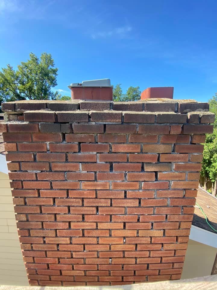 Brick chimney with damaged top section, against a blue sky.