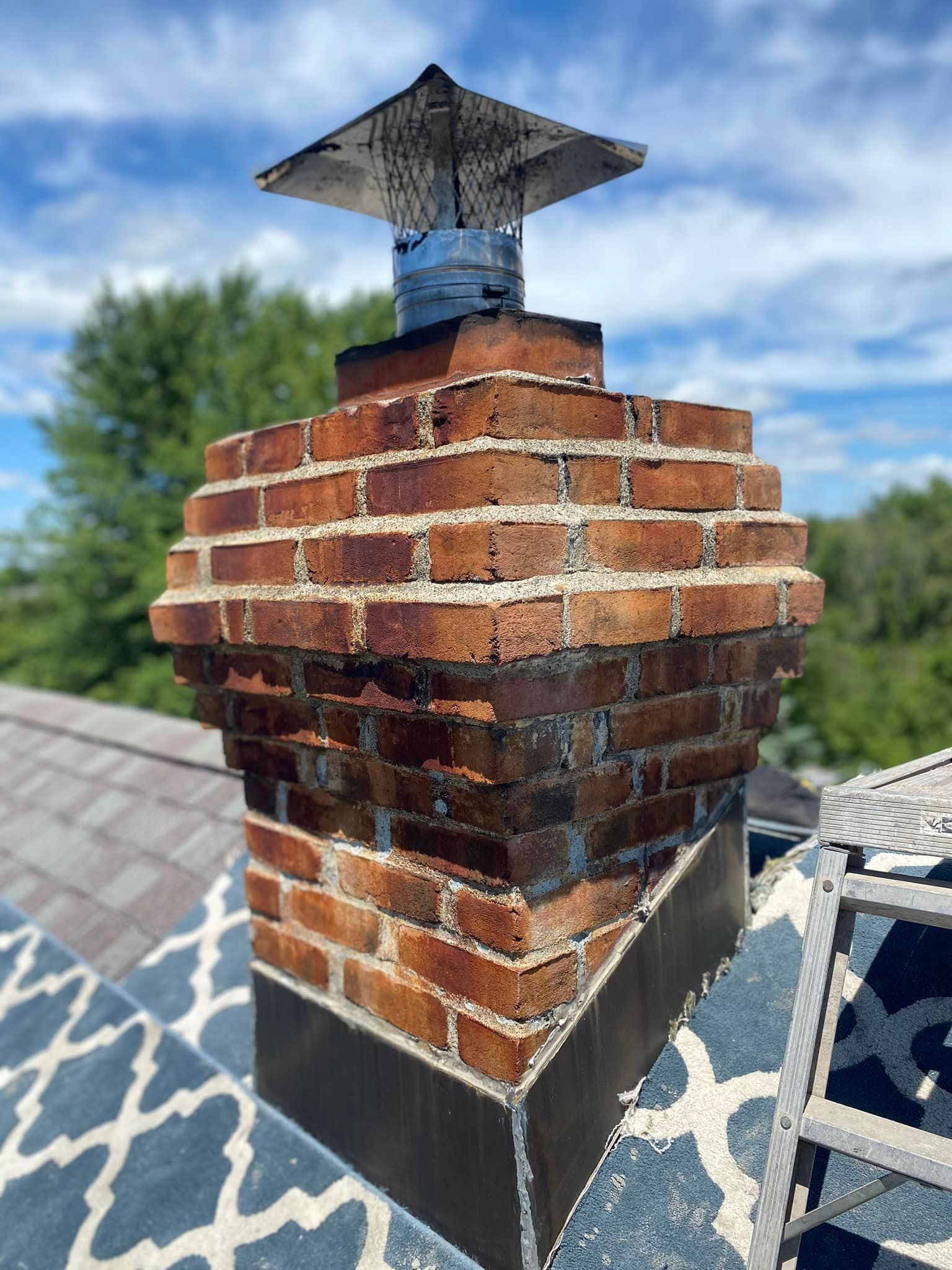 Brick chimney with metal cap on a rooftop, with a blue sky background.
