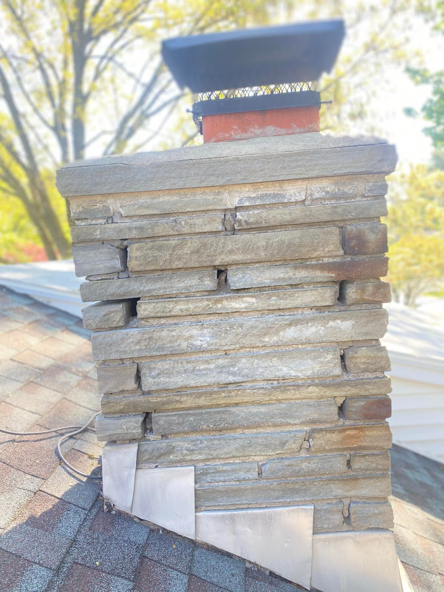 Stone chimney on a rooftop with a metal cap and flashing.