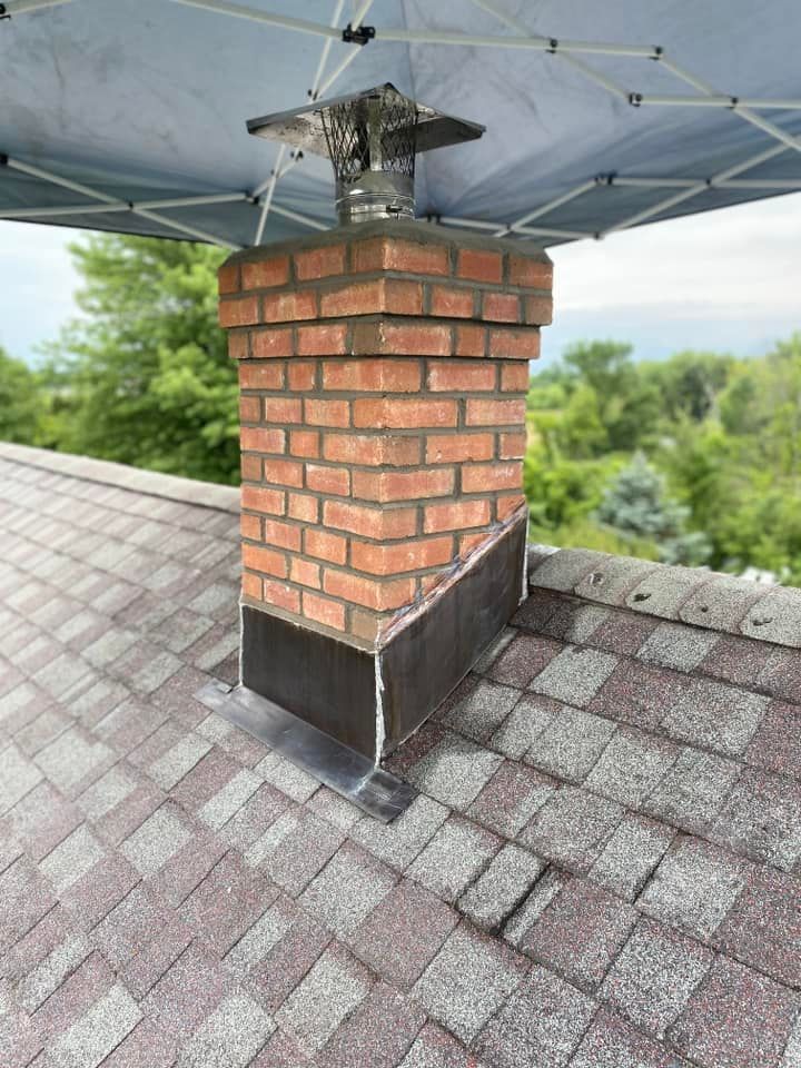 Brick chimney on a shingle roof with a metal cap. Blue sky visible.