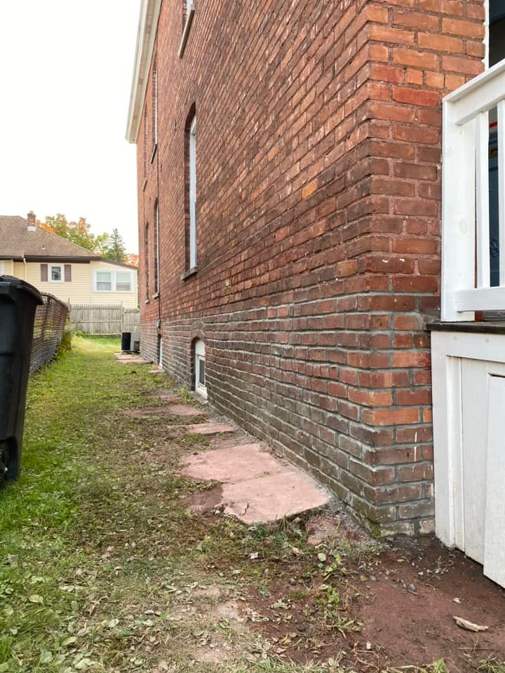 Brick building exterior with low foundation and pathway leading to small window.