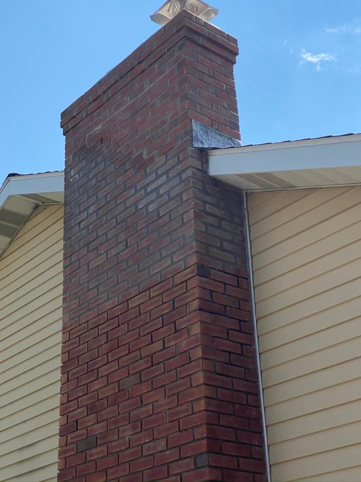 Brick chimney on a house with metal flashing, tan siding, and a blue sky.