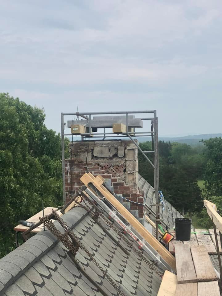 Rooftop chimney under construction, supported by scaffolding. A person is working on the roof with tools.