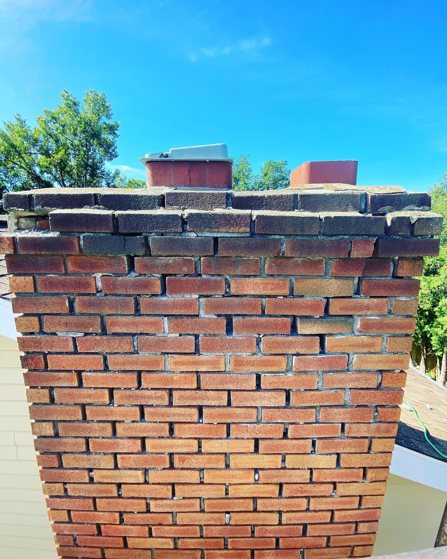 Brick chimney with damaged top against a blue sky, trees in background.