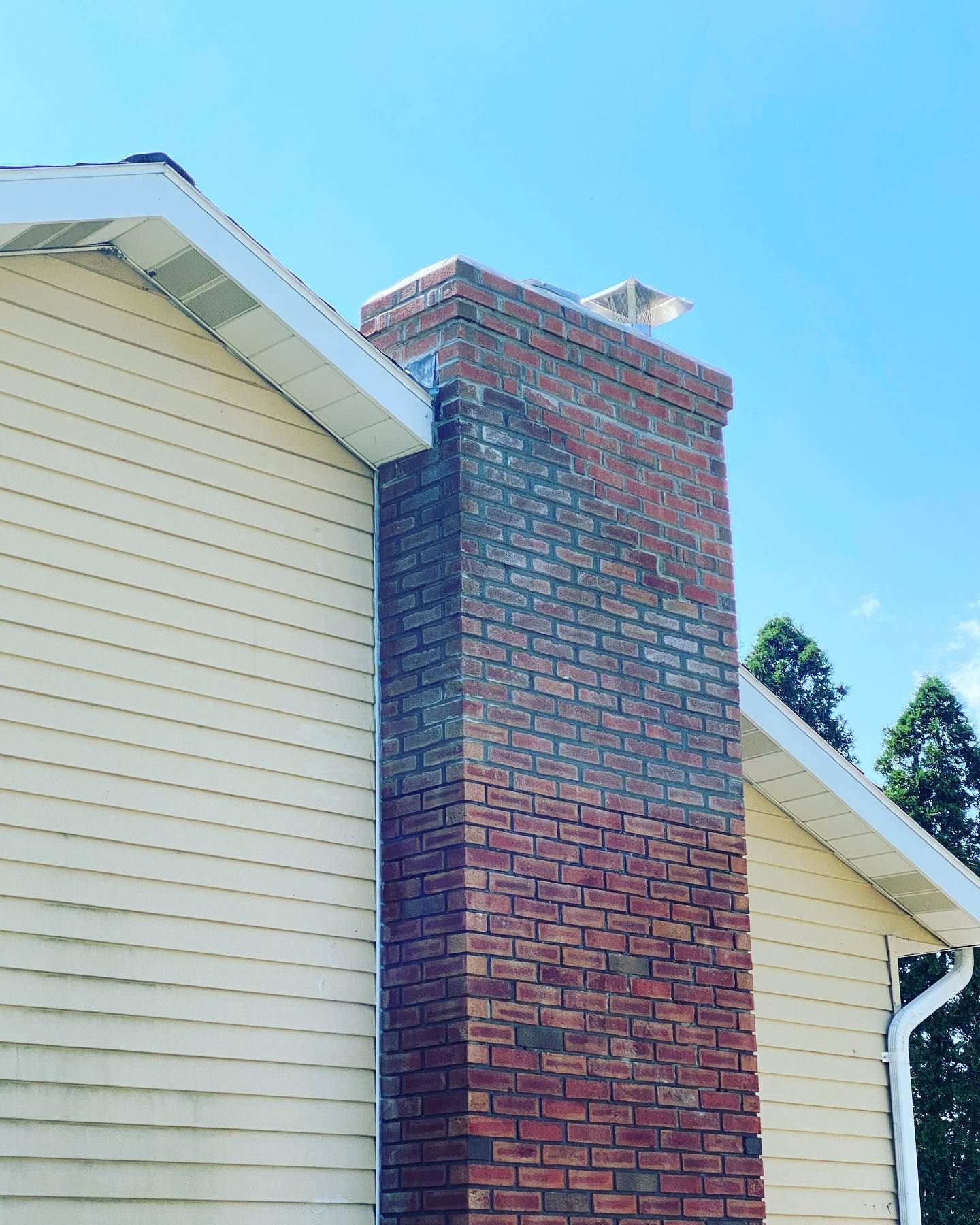 Brick chimney on a house, with tan siding, against a blue sky.