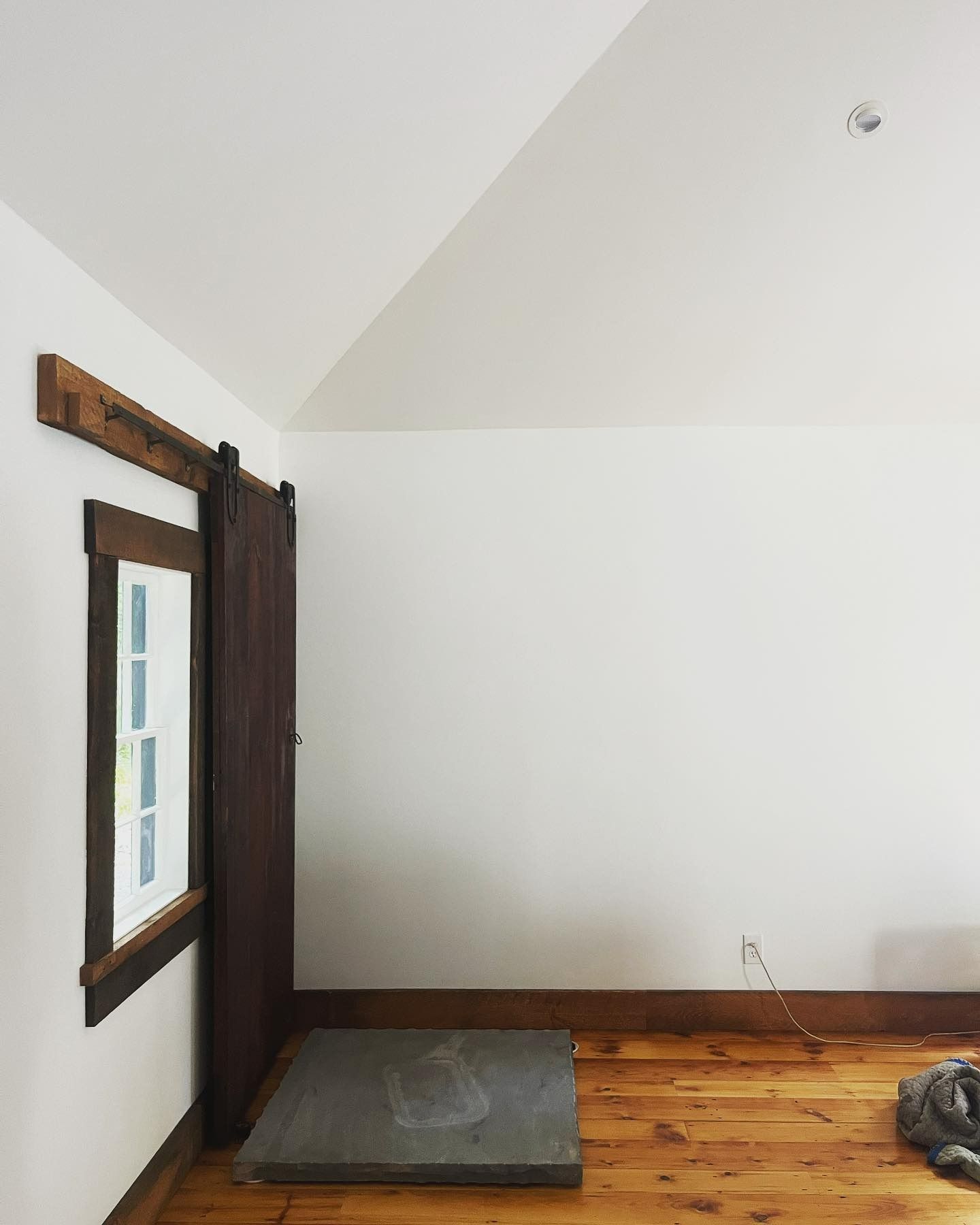 Room with wood floor, white walls, window with wood trim, and a sliding barn door.