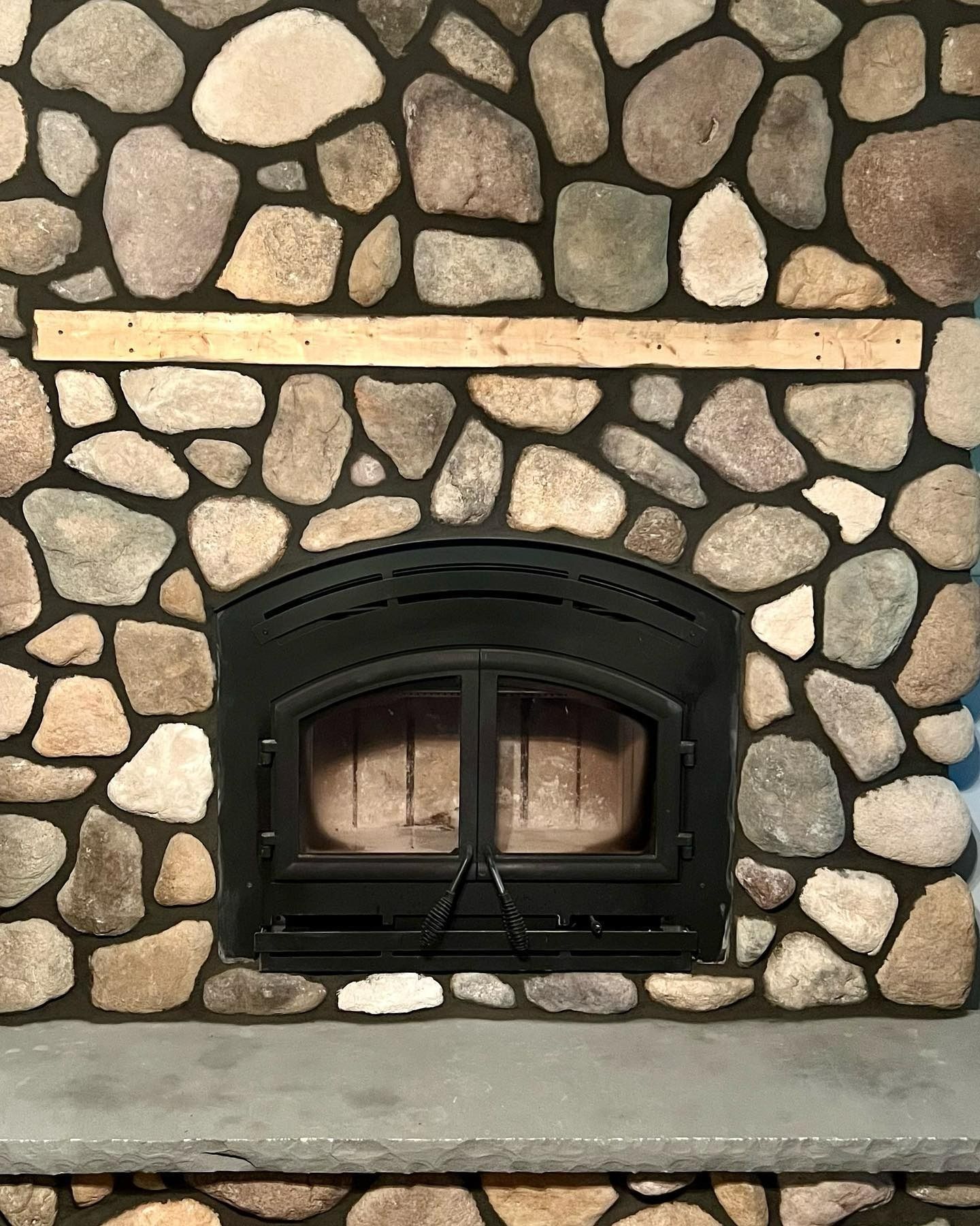 Fireplace with black metal doors set in a stone wall with a wooden beam above.
