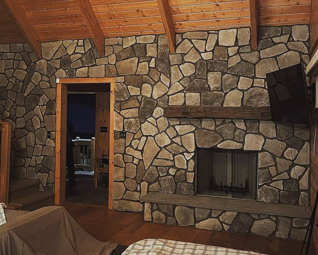 Cozy living room with stone walls, fireplace, wooden ceiling, and an open doorway.