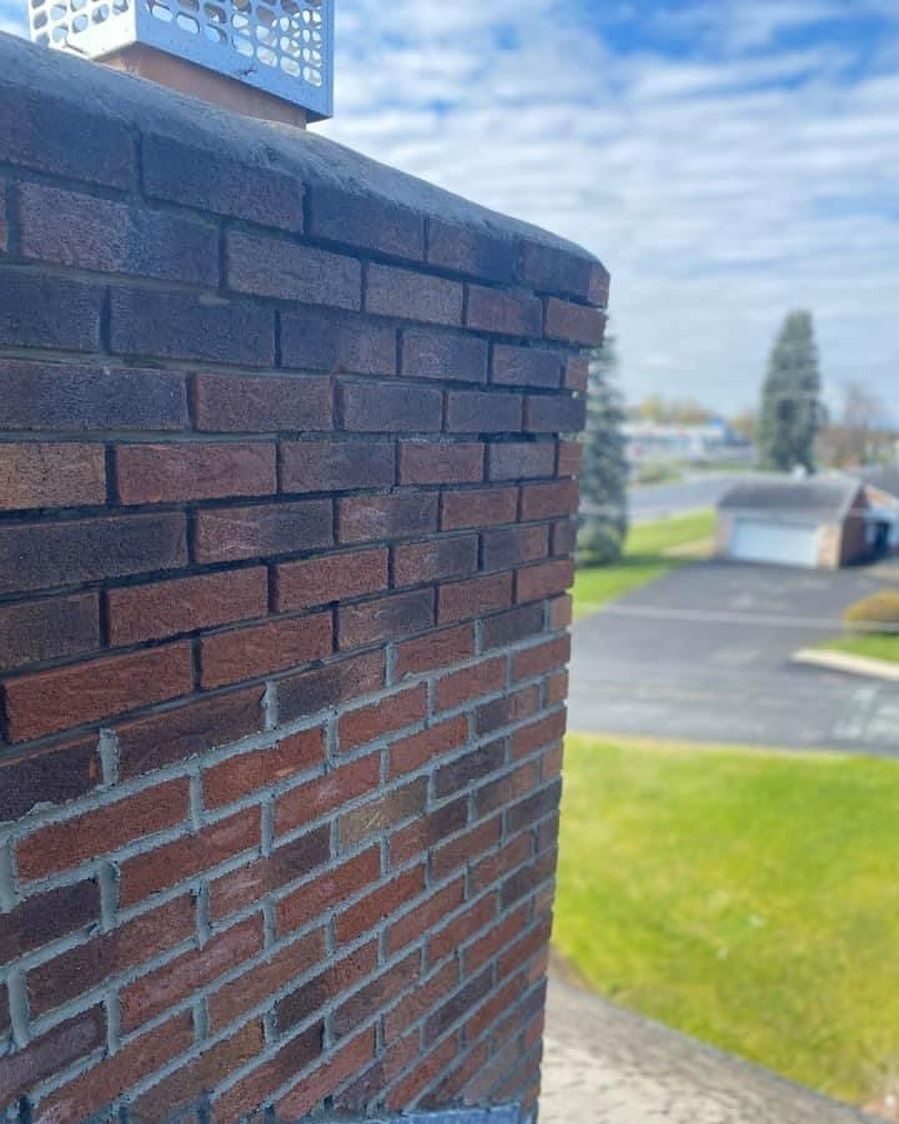 Brick chimney with dark and red bricks against a blurry outdoor background.