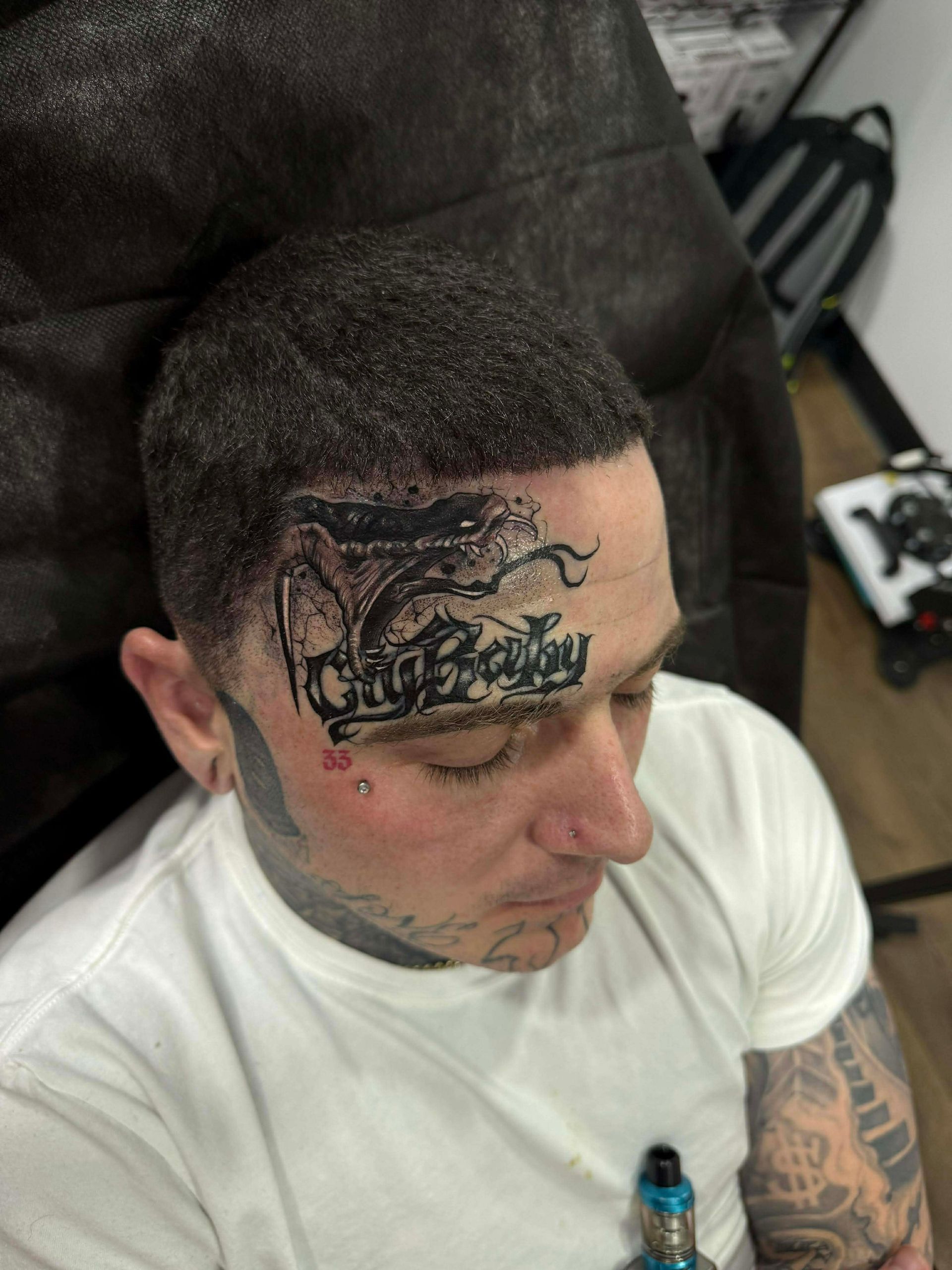 Man with face tattoos, including script across forehead and a red mark near the eye.