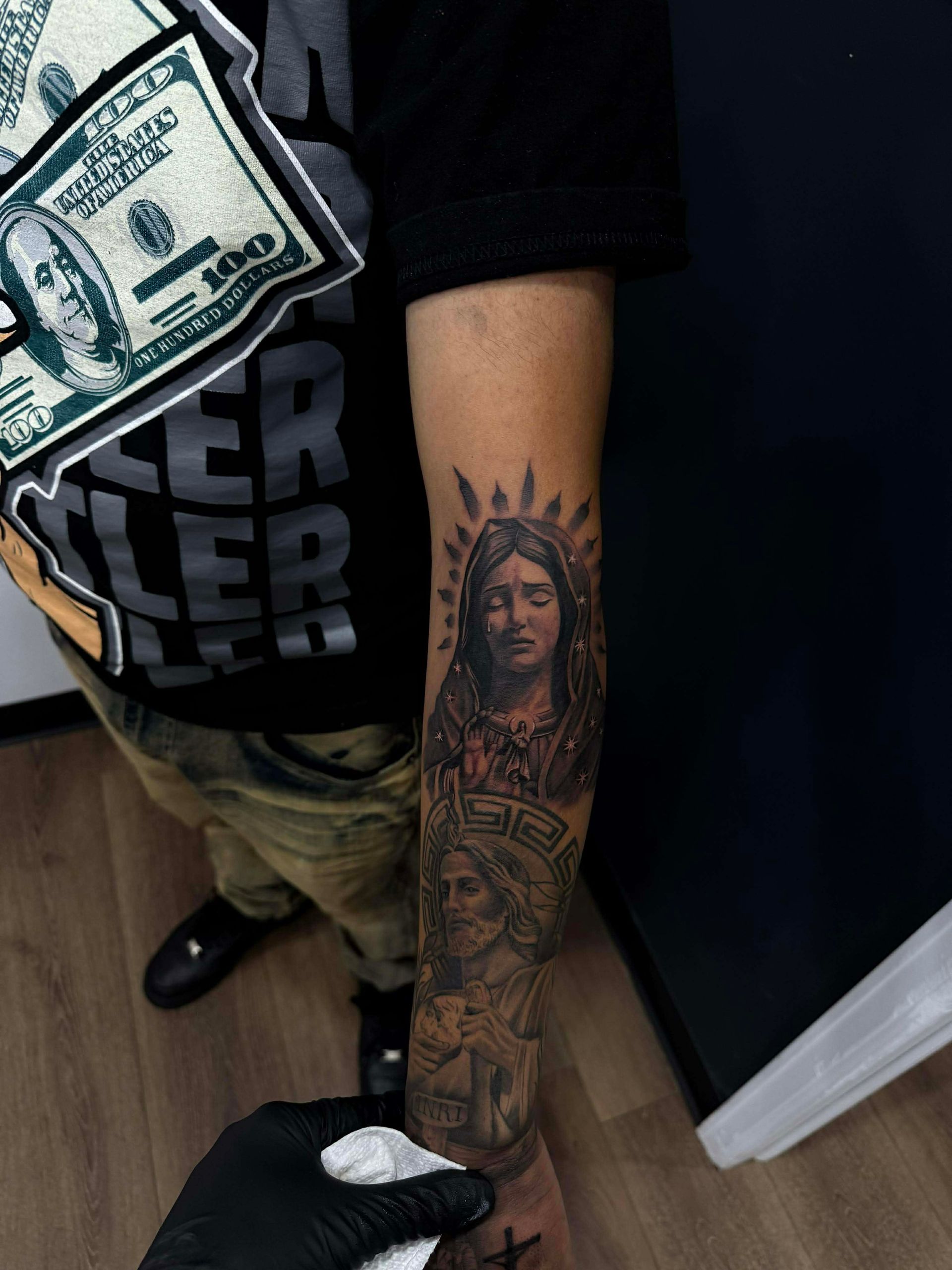 Person's arm with a detailed tattoo of a woman and money; holding a money-themed item. Black glove in view.