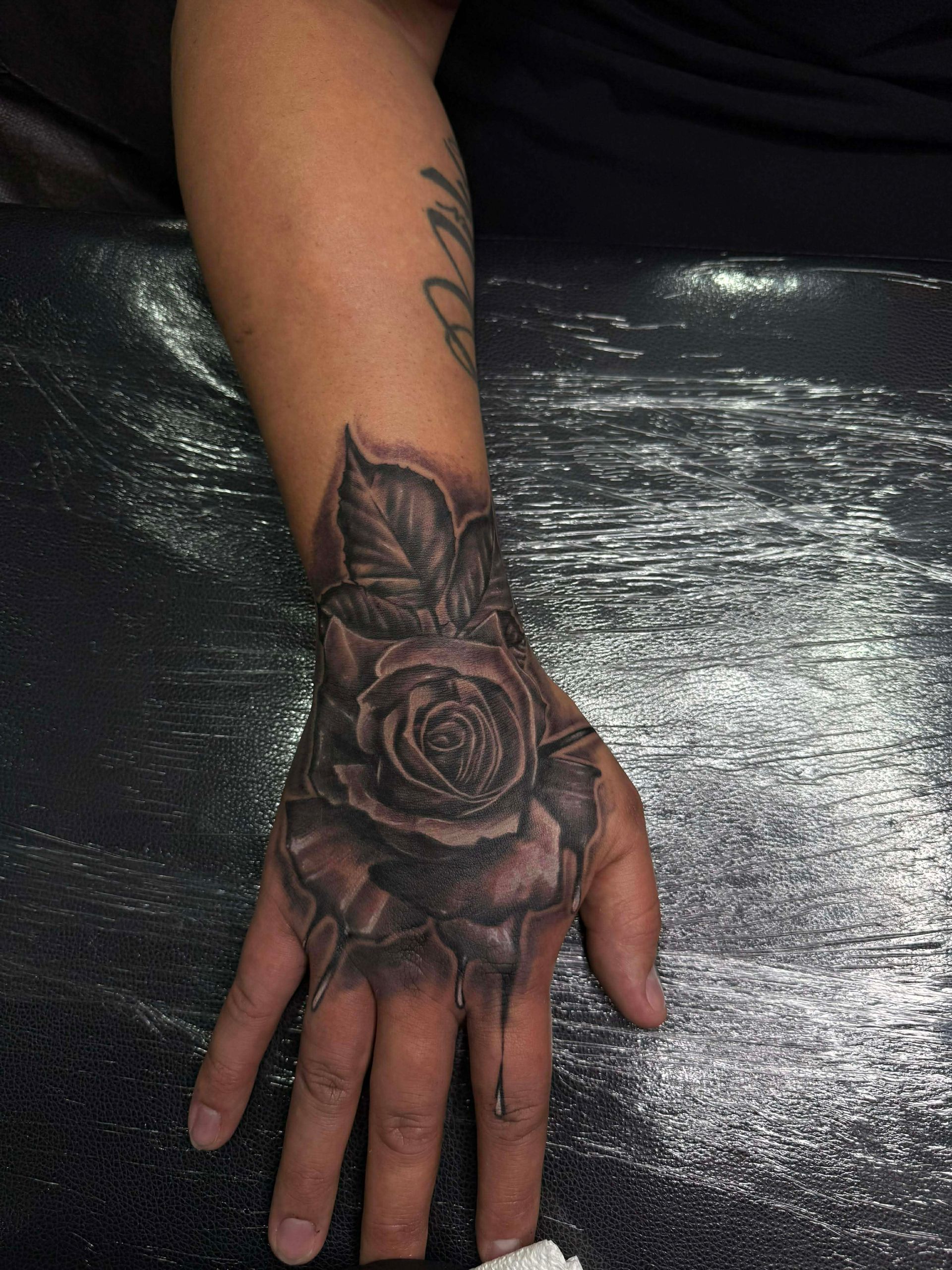 Black and gray rose tattoo on a hand, with leaves and shading.