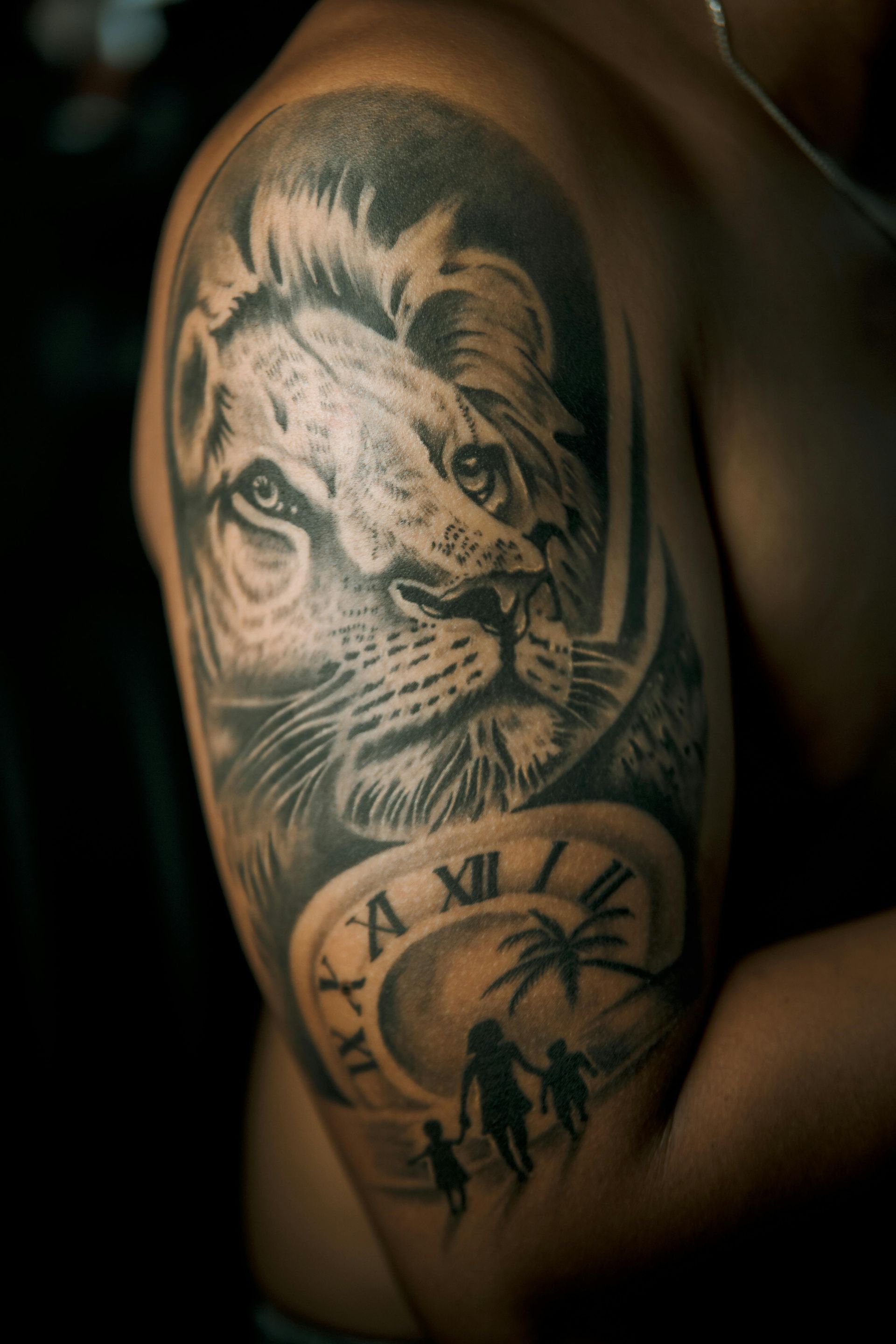 Lion and clock tattoo on arm; includes palm trees and figures.