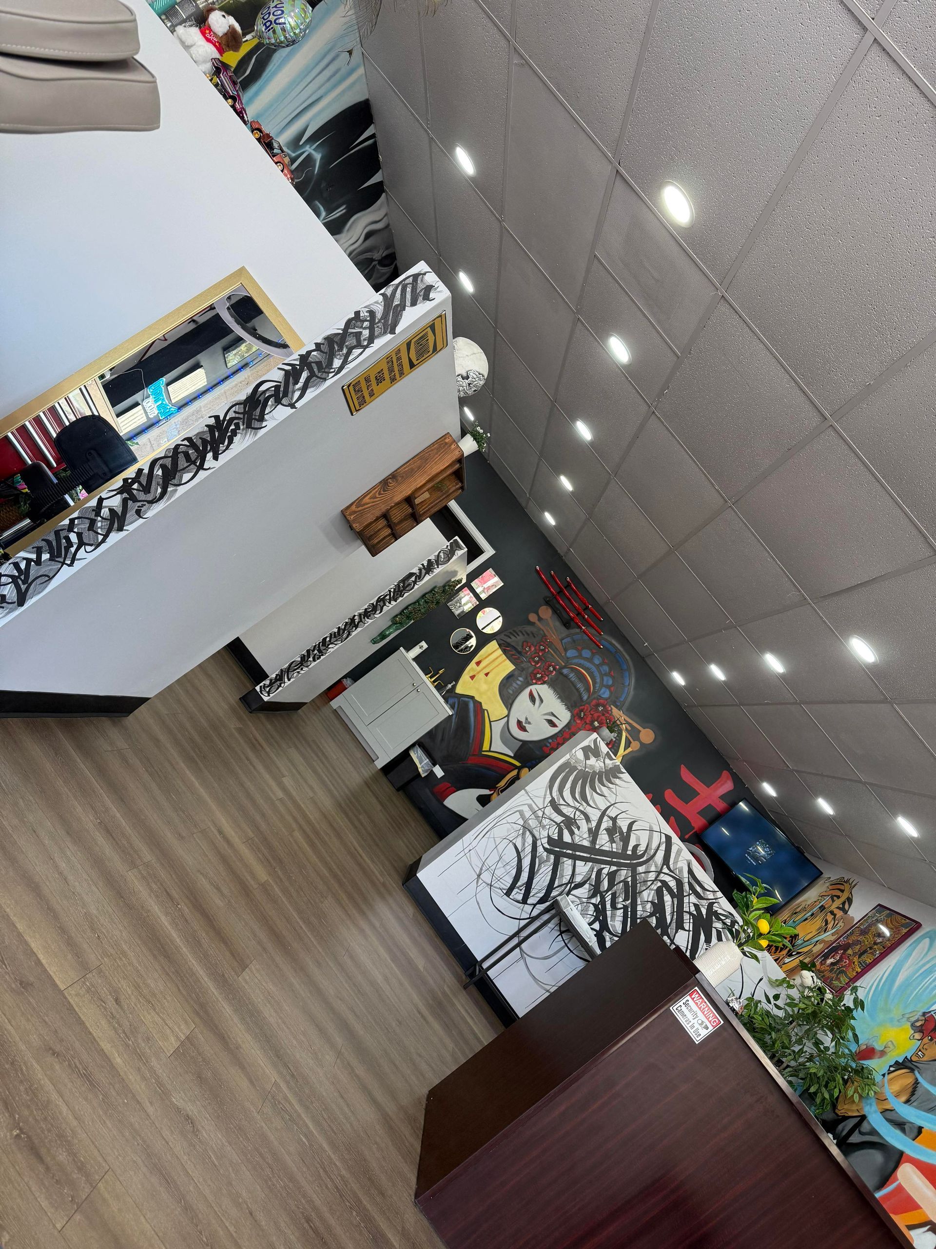 Man with arm tattoo smiling, standing in front of a colorful graffiti wall. He wears glasses and a tank top.