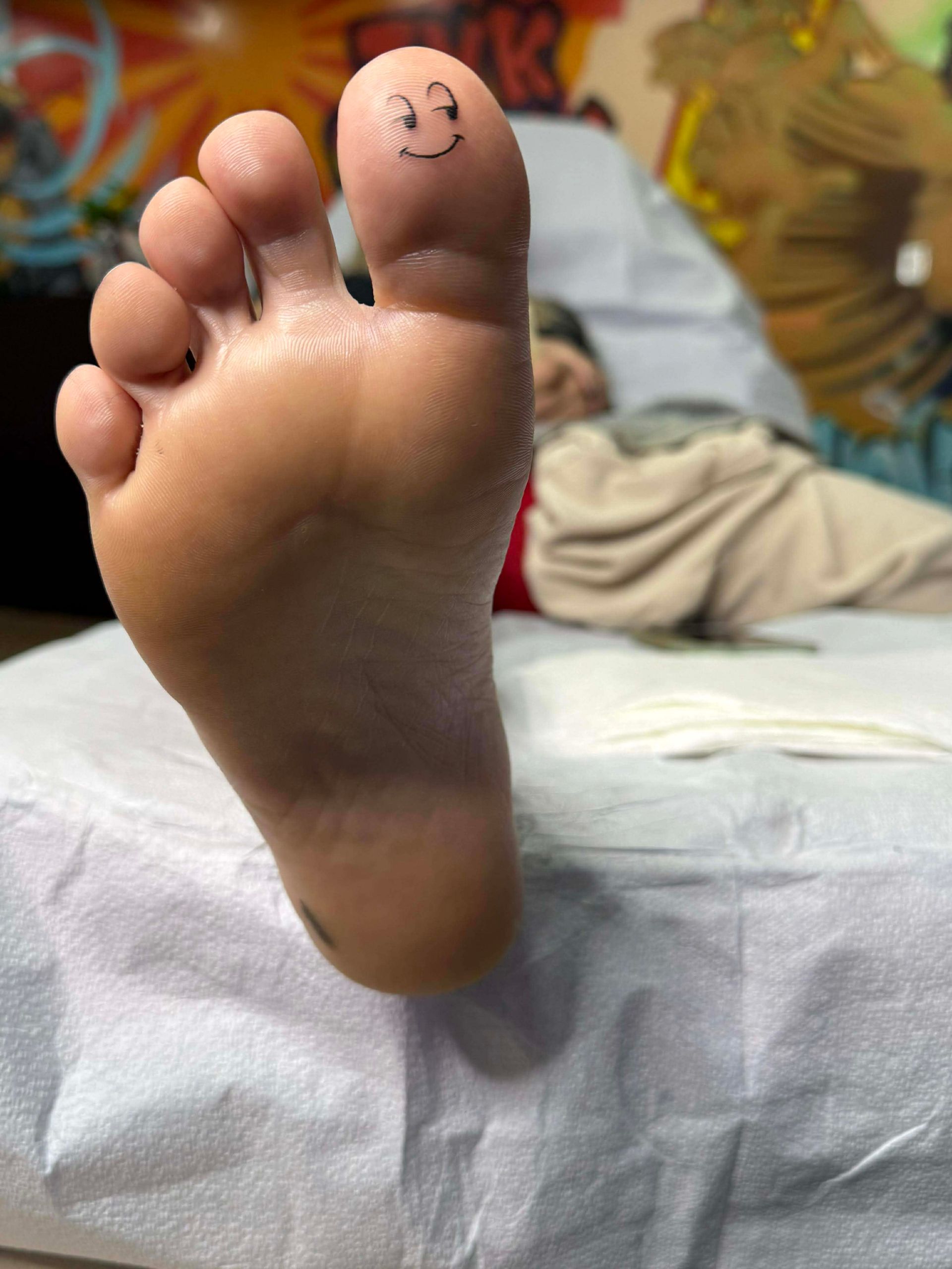 Foot with a smiley face tattoo on the big toe, lying on a white paper.
