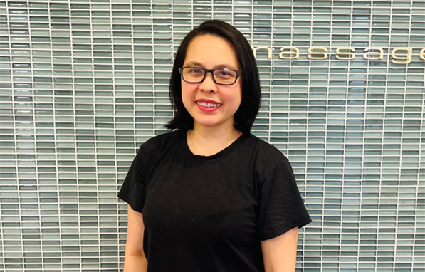 A woman wearing glasses and a black shirt is standing in front of a tiled wall.