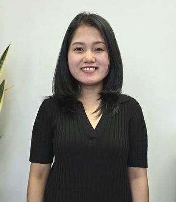 A woman in a black shirt is standing in front of a white wall.