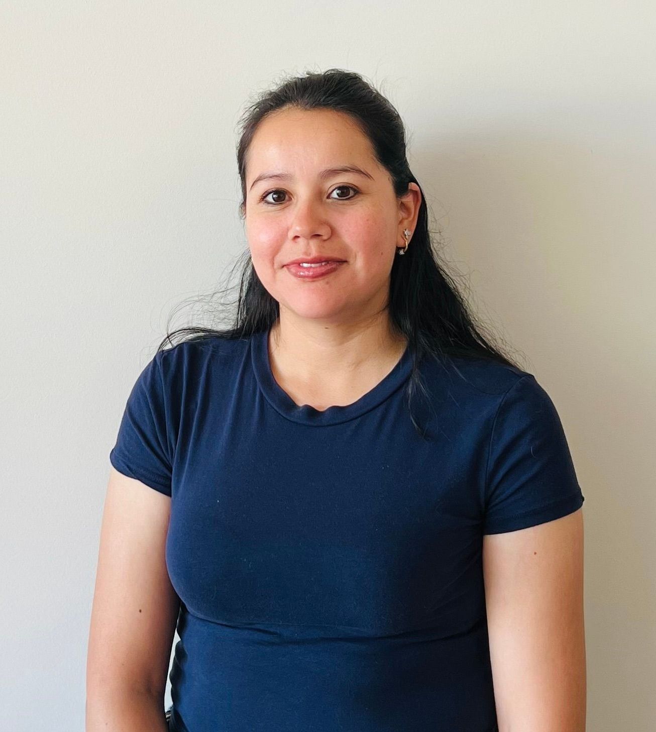 A woman in a blue shirt is standing in front of a white wall.