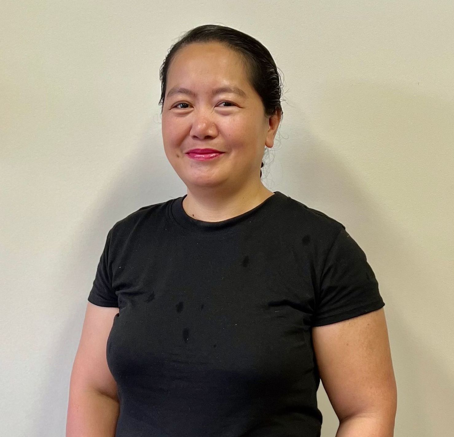 A woman in a black shirt is standing in front of a white wall.
