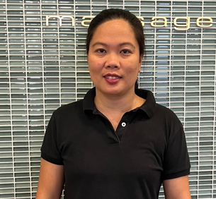 A woman in a black shirt is standing in front of a tiled wall.