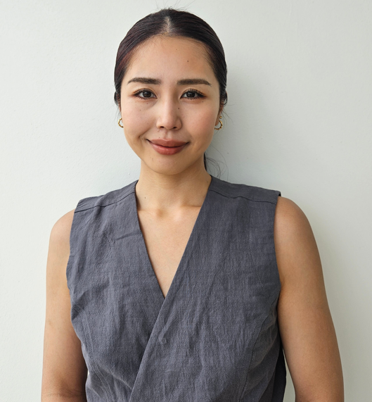 A woman in a grey sleeveless top is smiling for the camera