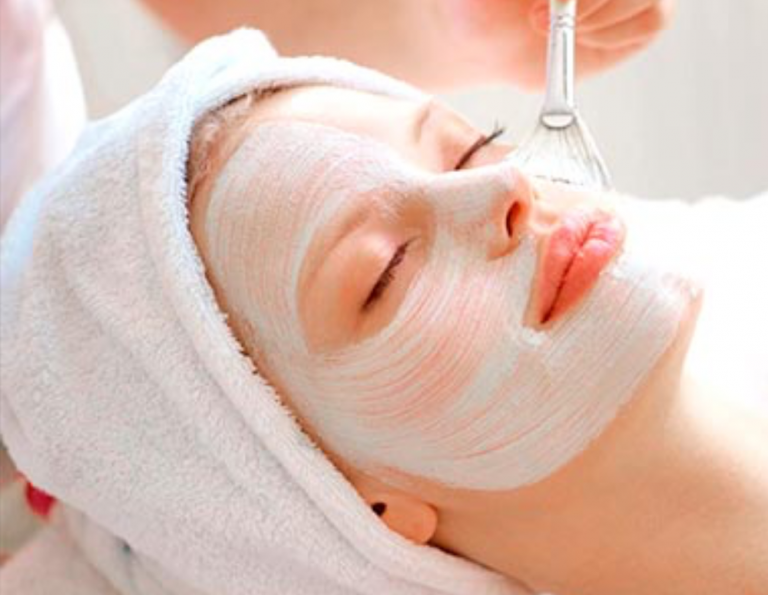 A woman is getting a facial treatment with a white mask on her face.