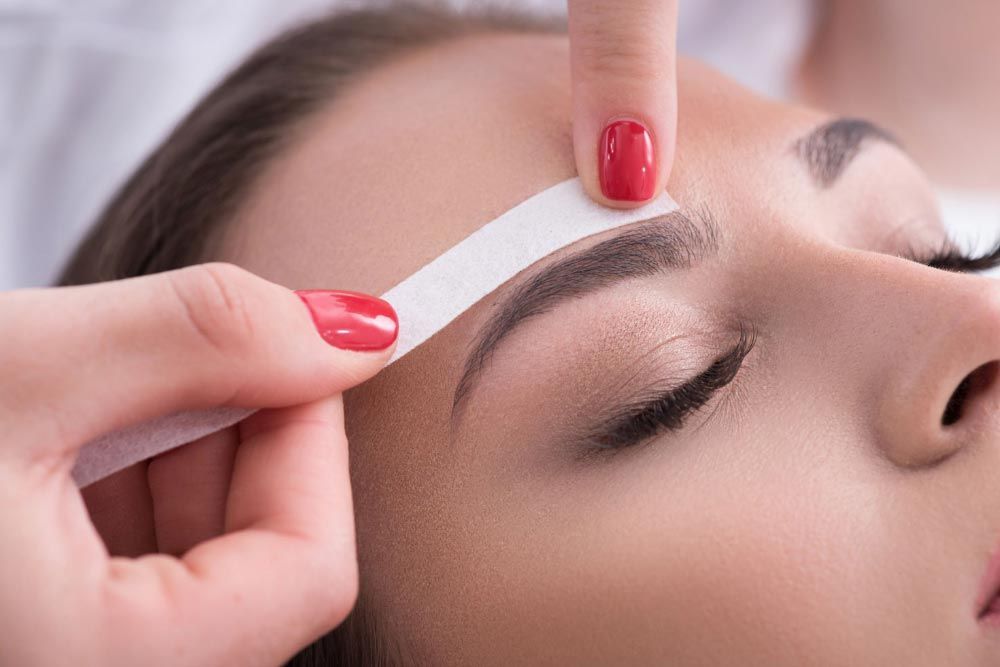 A woman with red nails is getting her eyebrows waxed.