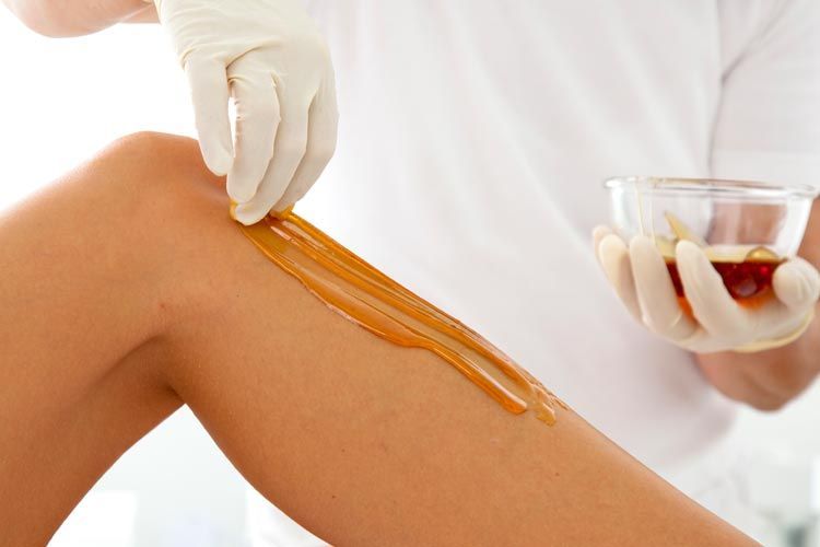 A woman is getting a sugaring treatment on her leg.