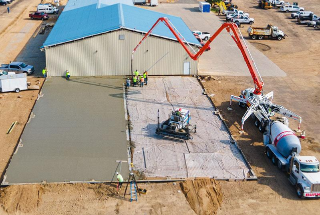 “Aerial view of a large slab pour beside a warehouse with a pump truck and crew during work by a concrete contractor in Oro Valley, AZ”