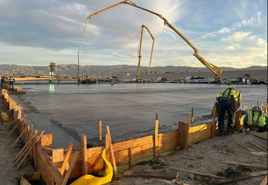 “Workers guiding a long pump hose to pour a wide concrete slab inside wood forms during a concrete contractor project in Oro Valley, AZ”