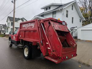 A red garbage truck is parked on the side of the road in front of a white house.