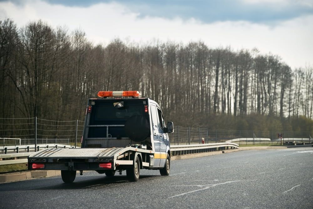 A Tow Truck Is Driving Down A Highway Next To A Forest — Ollies Towing & Shipping Container Sales in Durong, QLD