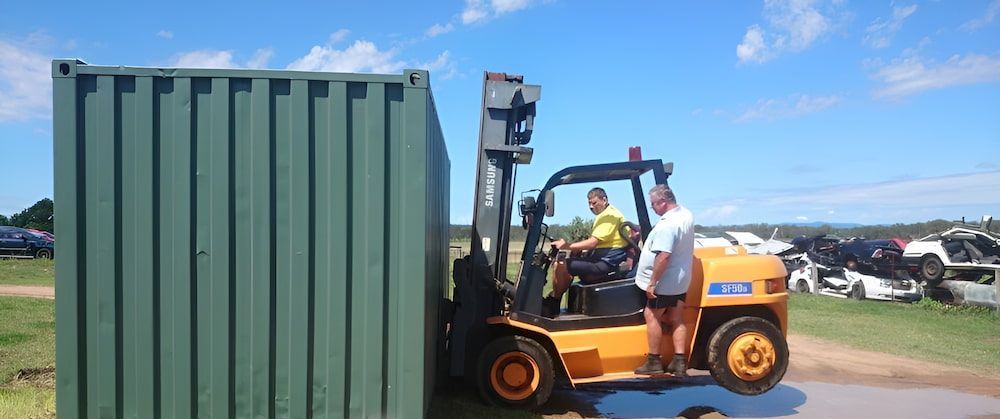 A Forklift Is Moving A Green Container In A Field — Ollies Towing & Shipping Container Sales in Kingaroy, QLD
