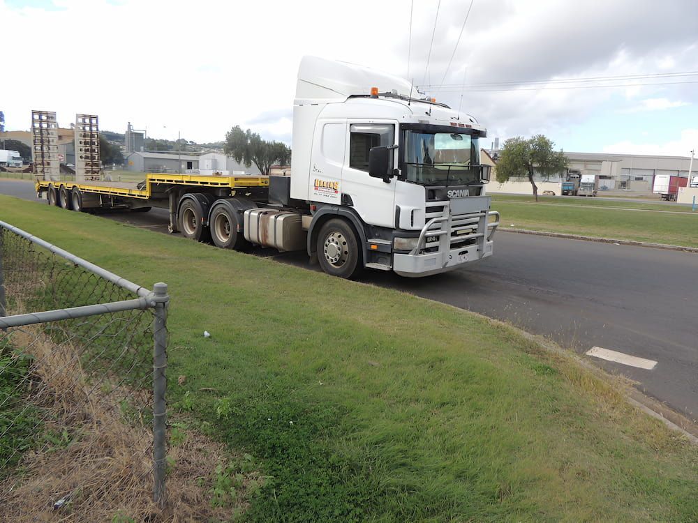 A White Truck With A Yellow Trailer Is Driving Down The Road — Ollies Towing & Shipping Container Sales in Kingaroy, QLD