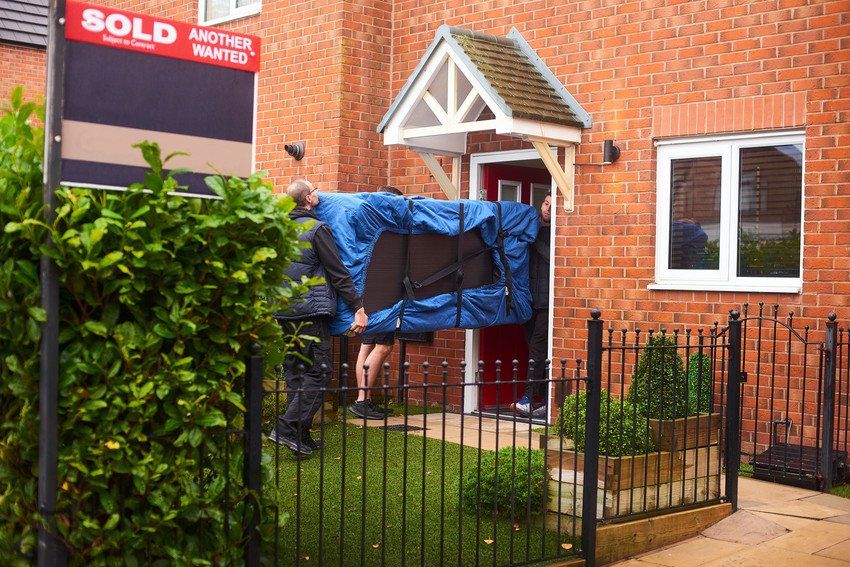 People carrying furniture into house with sold sign outside