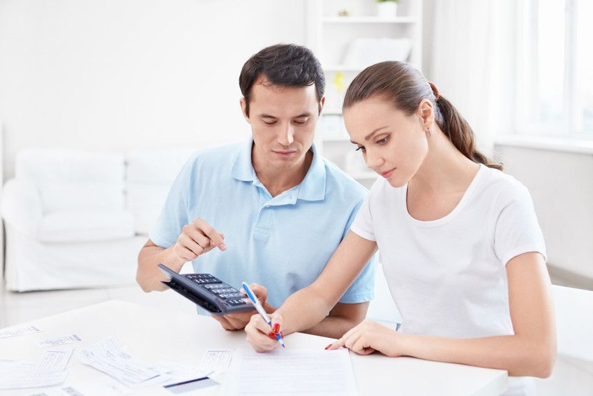 a man and a woman are sitting at a table looking at a calculator .