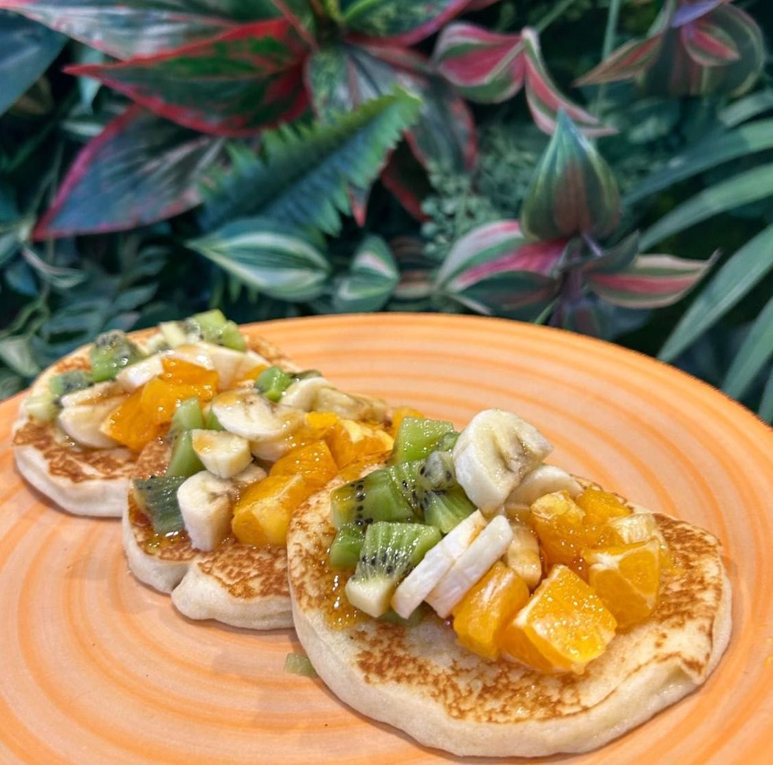 Tre pancake con banane, kiwi e arance su un piatto arancione