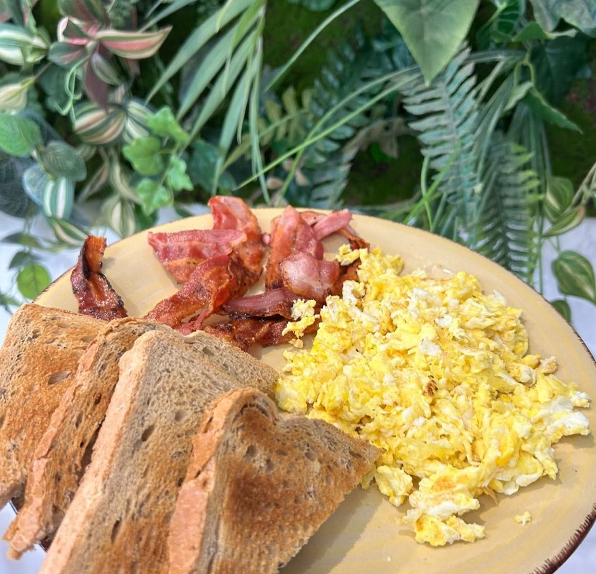 Un piatto di uova strapazzate, pane tostato e bacon su un tavolo