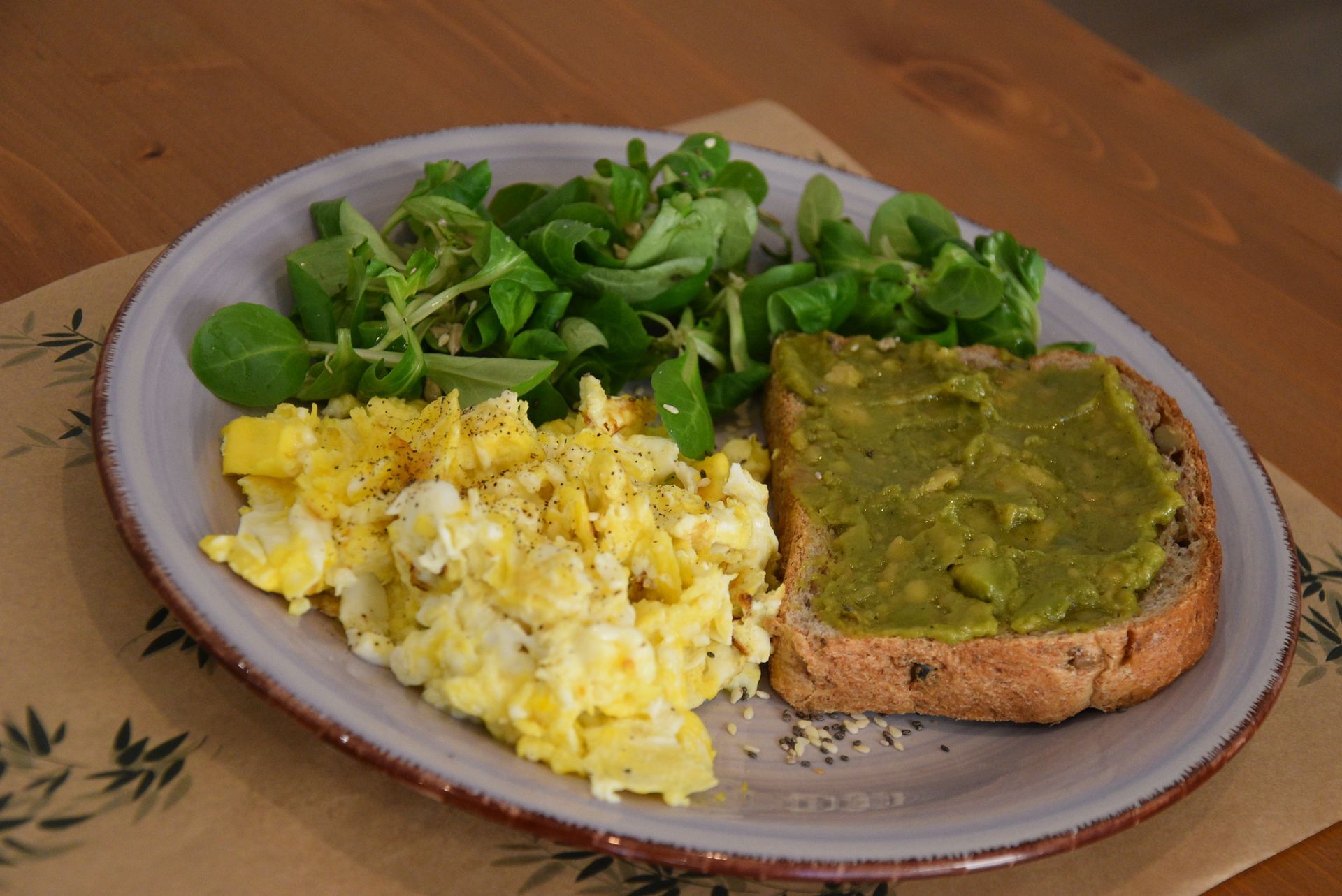 Un piatto di cibo con uova strapazzate, toast all'avocado e un'insalata su un tavolo.