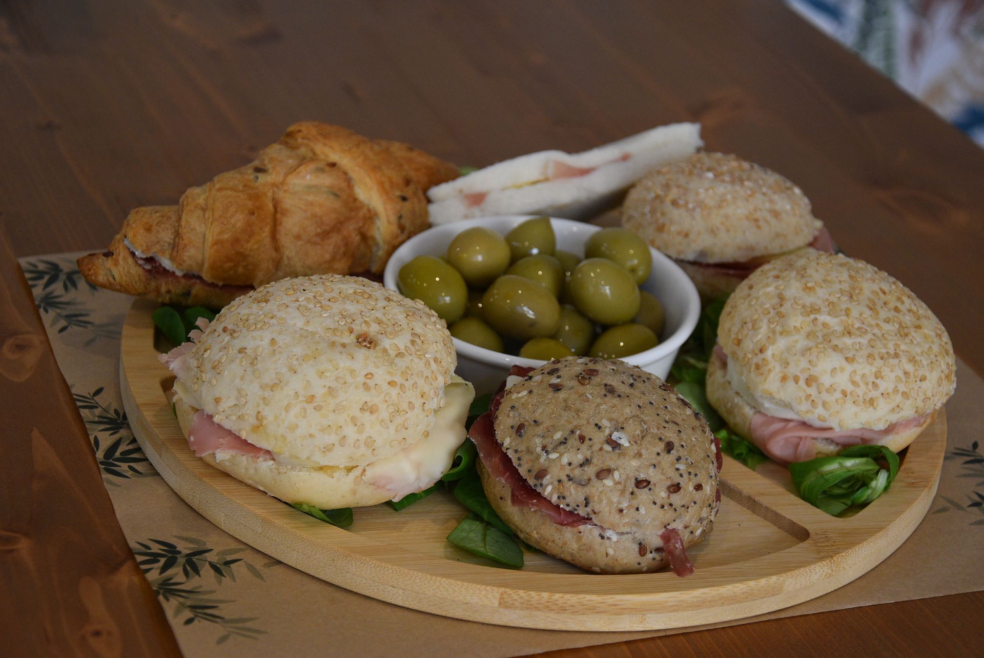 Un vassoio di legno pieno di panini e olive su un tavolo.
