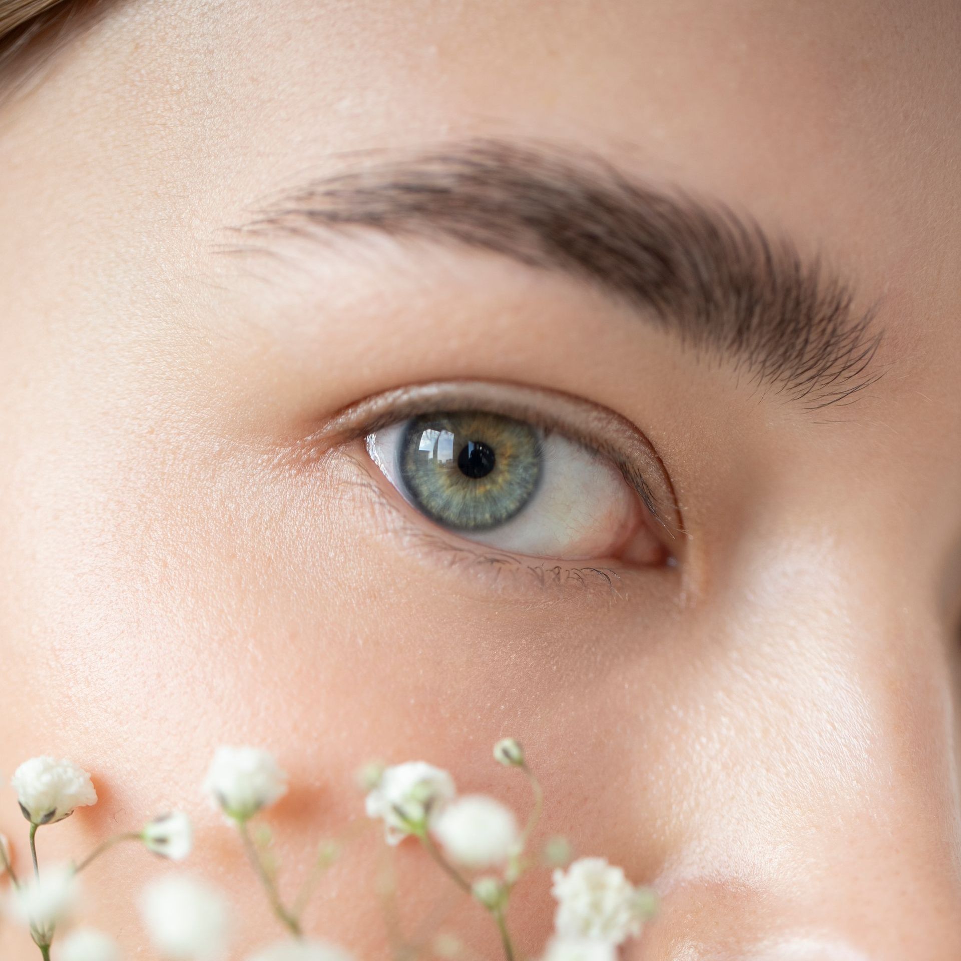 a close up of a woman 's eye with flowers in the foreground at ERA Wellness Spa in Georgetown, KY