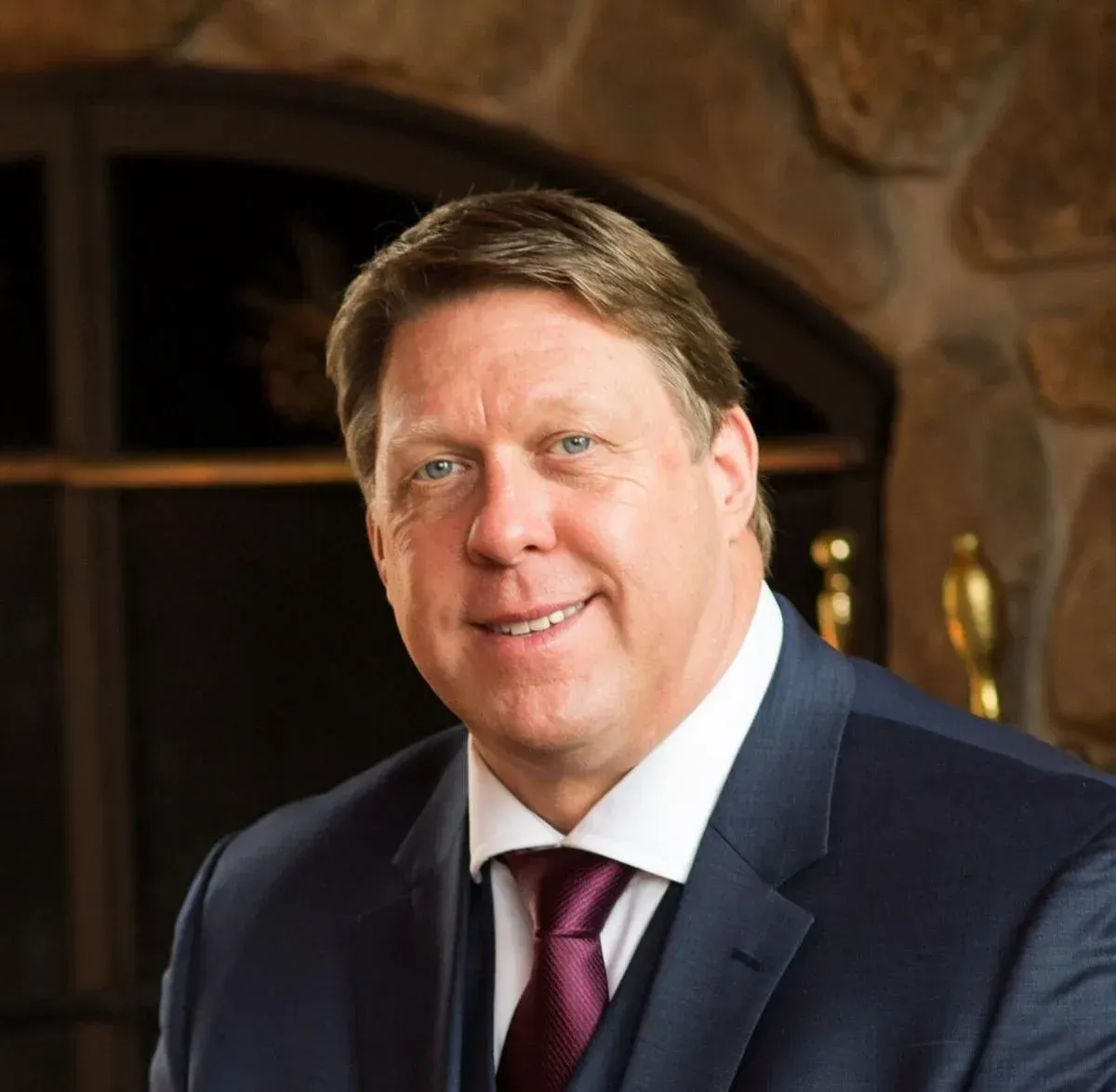 A man in a suit and tie is smiling in front of a fireplace
