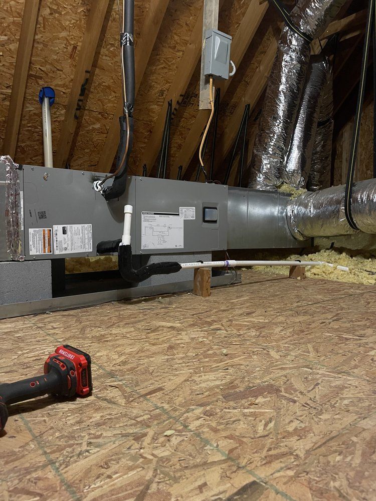 A drill is sitting on the floor in an attic next to a ventilation system.