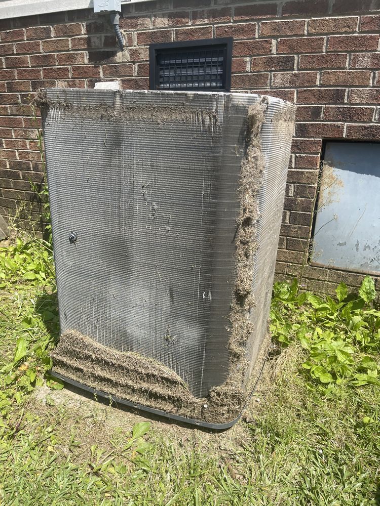 A dirty air conditioner is sitting in the grass in front of a brick building.